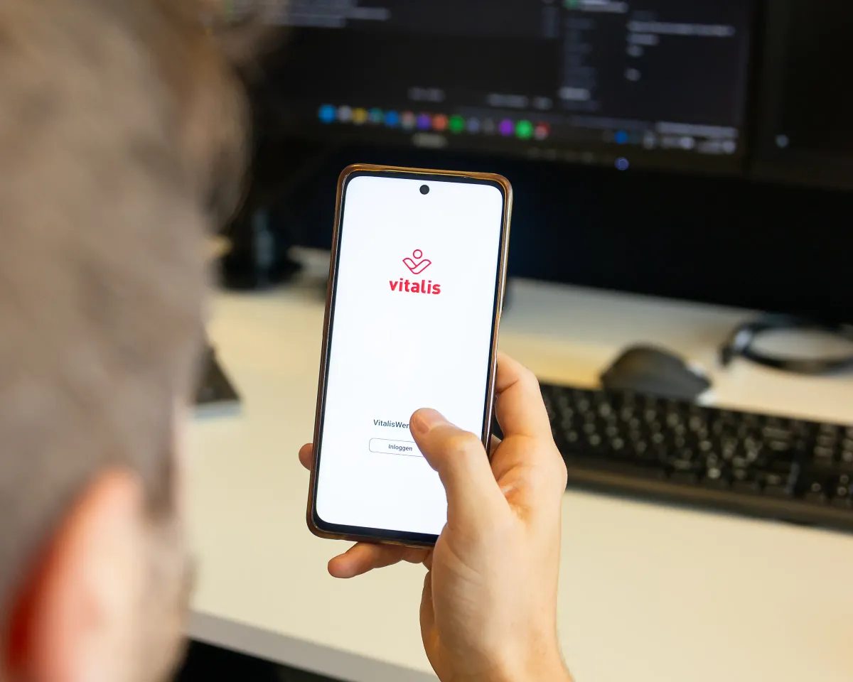 Een ontwikkelaar test een zorgapplicatie op zijn telefoon, met de code ernaast op het scherm.