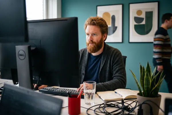 Een medewerker aan een bureau werkt geconcentreerd op één scherm terwijl er meerdere naast staan.