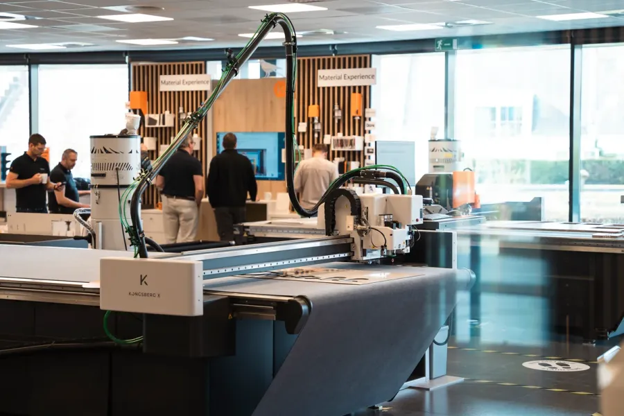Een Kongsberg X digitale snijtafel in het customer experience center van Kongsberg PCS in Gent, met bezoekers op de achtergrond.