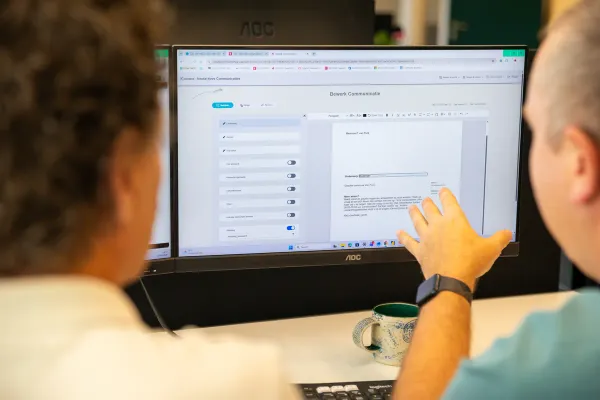 Een medewerker wijst op het scherm een tekstblok aan in het bewerkscherm van CustomerConnect, terwijl een collega meekijkt.