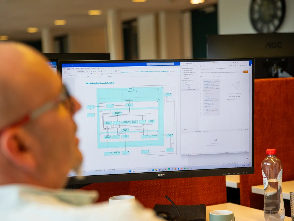 Een collega kijkt naar een architectuurplaat van een applicatielandschap op zijn scherm, met de API-calls ernaast.