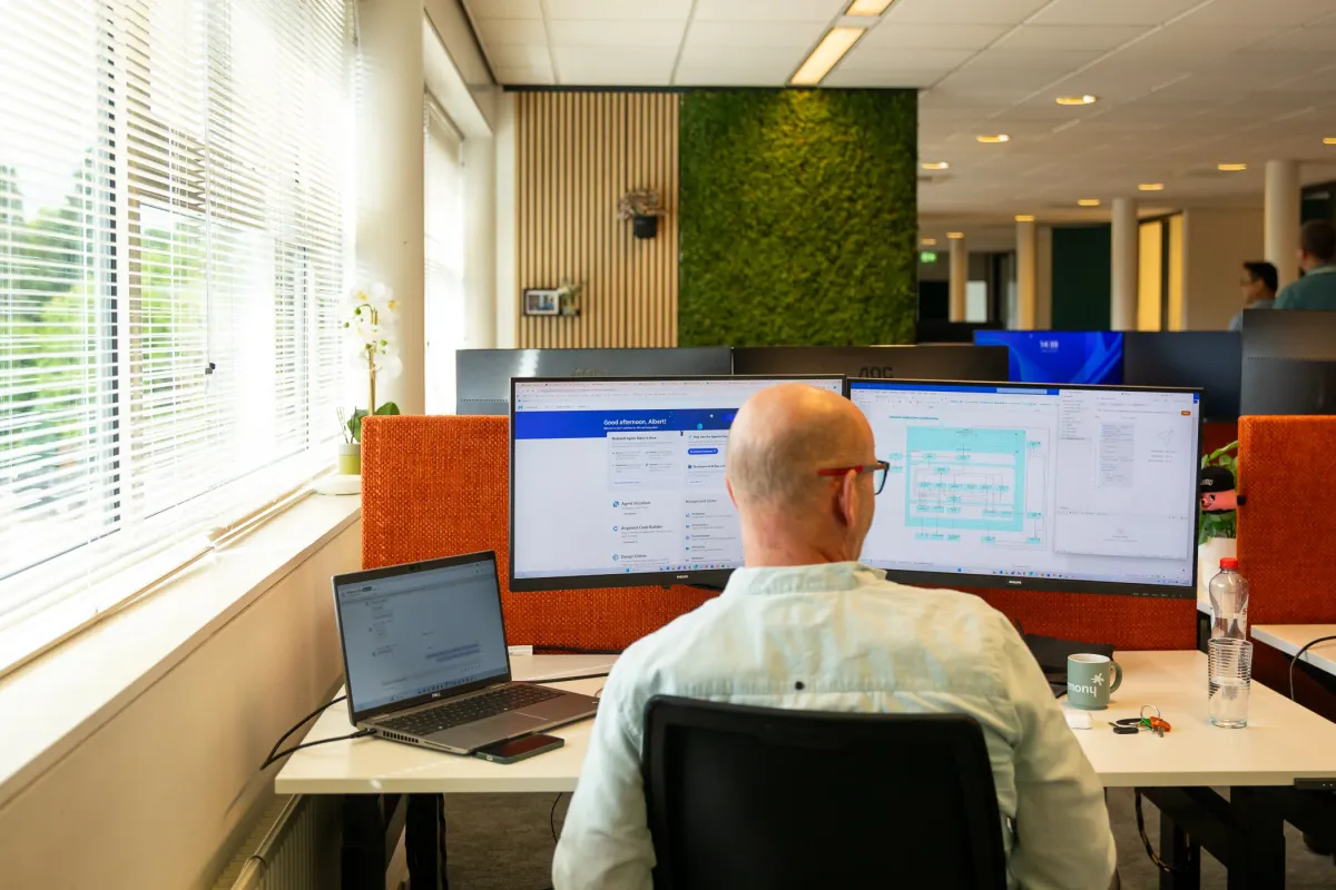 Een Harmony-collega werkt aan twee schermen, met MuleSoft Agent Fabric op het ene en een procesdiagram op het andere.