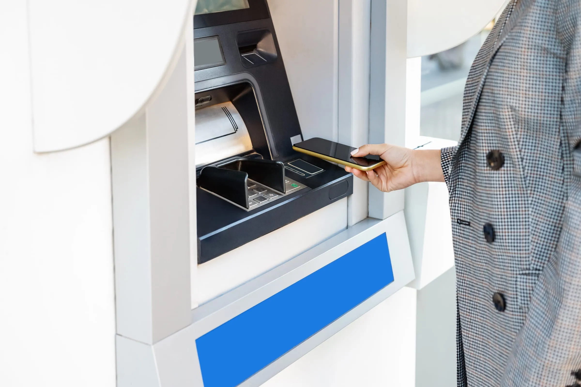 Een vrouw betaalt contactloos met haar smartphone aan een geldautomaat.